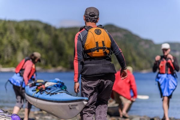 A group of people carrying kayaks down to the ocean in Coastal BC