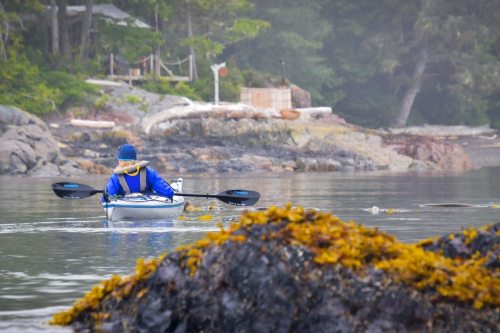 A kayaker paddling towards an oceanfront hot tub in Blackfish Sound