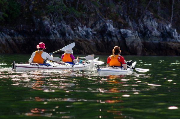 A group of three kayakers paddling close to the shoreline in Desolation Sound