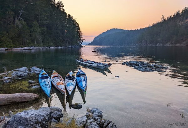 Six empty kayaks floating in a bay at sunset in Coastal BC